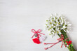 White wooden background with a bouquet of snowdrop flowers and red and white martenitsa for the holiday of March 1, copy space.