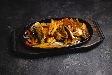 Wall Mural - Fried fish with vegetables in a frying pan on a dark background.