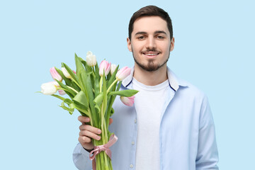 Wall Mural - Young man with bouquet of beautiful tulips on blue background. International Women's Day