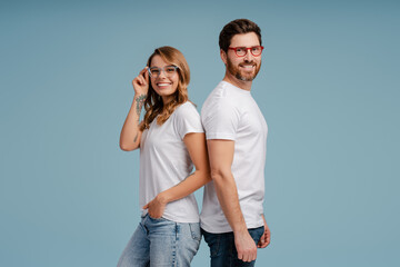 Portrait of attractive smiling man and woman wearing white t shirt and stylish eyeglasses isolated on blue background. Happy confident fashion models posing for pictures in studio