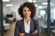 Business woman. Portrait of a african american, beautiful, young and happy woman in a suit standing in a modern office. Smiling female manager looking at the camera in a workplace