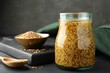 Whole grain mustard in jar and dry seeds on black wooden table