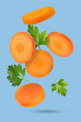 Wall Mural - Fresh carrot slices and green parsley falling on light blue background