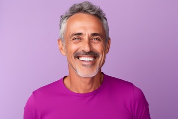 Portrait of a happy mature man with grey hair and beard smiling at camera while standing against purple background