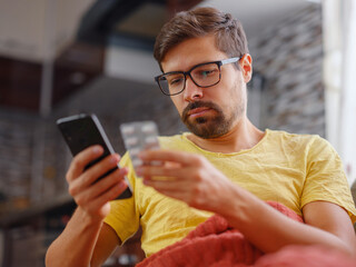 Young Caucasian man using smart phone for reading, searching prescription on bottle medicine, pill label text about information online, instructions side effects, pharmacy medicament concept