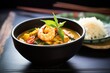 prawn curry in a black bowl on a bamboo mat