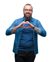 Sticker - Young caucasian hipster man wearing glasses over isolated background smiling in love showing heart symbol and shape with hands. Romantic concept.