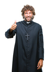 Wall Mural - Handsome hispanic catholic priest man over isolated background doing happy thumbs up gesture with hand. Approving expression looking at the camera with showing success.