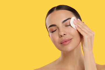 Wall Mural - Beautiful woman removing makeup with cotton pad on yellow background. Space for text