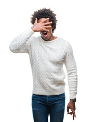 Poster - Afro american man over isolated background peeking in shock covering face and eyes with hand, looking through fingers with embarrassed expression.