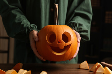 Wall Mural - Woman holding carved pumpkin for Halloween at wooden table, closeup