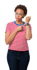 Wall Mural - Beautiful young african american woman wearing glasses over isolated background In hurry pointing to watch time, impatience, upset and angry for deadline delay