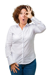 Canvas Print - Beautiful middle ager senior businees woman over isolated background doing ok gesture shocked with surprised face, eye looking through fingers. Unbelieving expression.