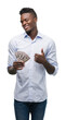 © Krakenimages.com - Young african american businessman holding dollars happy with big smile doing ok sign, thumb up with fingers, excellent sign