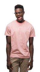 Sticker - Young african american man wearing pink t-shirt sticking tongue out happy with funny expression. Emotion concept.