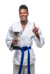 Poster - Young african american man over isolated background wearing kimono holding trophy surprised with an idea or question pointing finger with happy face, number one