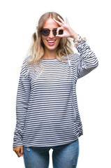 Sticker - Beautiful young blonde woman wearing headphones and sunglasses over isolated background doing ok gesture with hand smiling, eye looking through fingers with happy face.