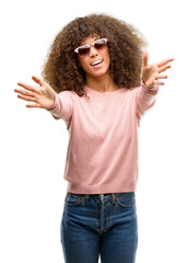 Poster - African american woman wearing pink sunglasses looking at the camera smiling with open arms for hug. Cheerful expression embracing happiness.