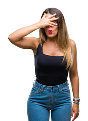 Wall Mural - Young beautiful woman over isolated background peeking in shock covering face and eyes with hand, looking through fingers with embarrassed expression.