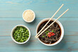Tasty buckwheat noodle (soba) soup with chili pepper, green onion, sesame and chopsticks on light blue wooden table, flat lay