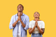 © Prostock-studio - Hopeful black couple with hands clasped, looking upwards, yellow background