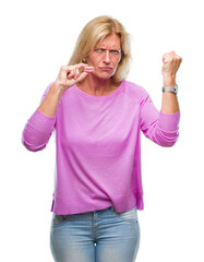 Canvas Print - Middle age blonde woman eatin pink macaron biscuit over isolated background annoyed and frustrated shouting with anger, crazy and yelling with raised hand, anger concept