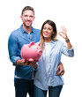 © Krakenimages.com - Young couple in love holding piggy bank over isolated background doing ok sign with fingers, excellent symbol