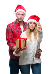 Poster - Young couple in love wearing christmas hat and holding present over isolated background with open hand doing stop sign with serious and confident expression, defense gesture