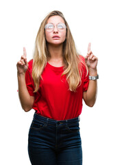 Sticker - Young beautiful blonde woman wearing glasses over isolated background amazed and surprised looking up and pointing with fingers and raised arms.