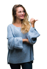 Sticker - Young beautiful blonde woman wearing sweater and glasses over isolated background smiling with happy face looking and pointing to the side with thumb up.