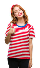 Sticker - Young beautiful woman over isolated background doing happy thumbs up gesture with hand. Approving expression looking at the camera with showing success.