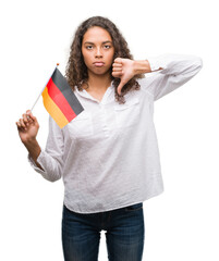 Sticker - Young hispanic woman holding flag of Germany with angry face, negative sign showing dislike with thumbs down, rejection concept