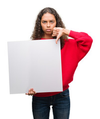 Wall Mural - Young hispanic woman holding blank banner with angry face, negative sign showing dislike with thumbs down, rejection concept