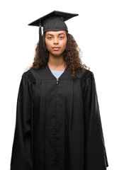 Wall Mural - Young hispanic woman wearing graduation uniform with a confident expression on smart face thinking serious