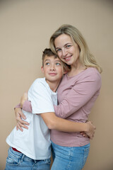 Wall Mural - cool young teenager boy with white t-shirt posing together with his beautiful mother in front of brown background