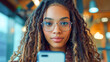 A young beautiful girl with long curly pigtail hair wearing glasses takes selfies while looking at her smartphone or just scrolling through the internet or social media.