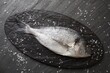 Fresh raw dorado fish and sea salt on black table, flat lay