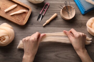 Woman felting from wool at wooden table, top view