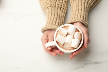 Wall Mural - Woman with cup of tasty hot chocolate and marshmallows at white marble table, top view. Space for text