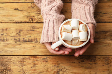 Wall Mural - Woman with cup of tasty hot chocolate and marshmallows at wooden table, top view. Space for text