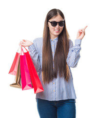 Sticker - Young Chinese woman over isolated background holding shopping bags on sales very happy pointing with hand and finger to the side