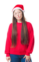 Sticker - Young Chinese woman over isolated background wearing christmas hat making fish face with lips, crazy and comical gesture. Funny expression.