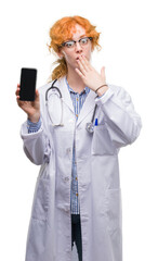 Poster - Young redhead doctor woman showing smartphone cover mouth with hand shocked with shame for mistake, expression of fear, scared in silence, secret concept