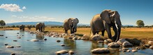 An Awe-inspiring Image Captures Three Majestic Elephants, With Wrinkled Skin And Trunks Raised High, Standing By A Serene Body Of Water As The Sky Above Is Filled With Fluffy White Clouds And Lush Gr