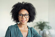 Cheerful young woman with curly hair and glasses smiling confidently, exuding positivity and professional ease.