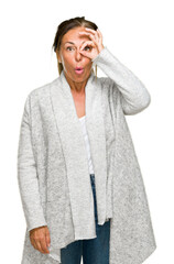 Sticker - Beautiful middle age adult woman wearing winter sweater over isolated background doing ok gesture shocked with surprised face, eye looking through fingers. Unbelieving expression.