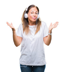 Wall Mural - Middle age hispanic woman listening to music wearing headphones over isolated background clueless and confused expression with arms and hands raised. Doubt concept.