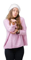 Poster - Young beautiful brunette woman wearing sweater and winter hat over isolated background looking at the camera blowing a kiss with hand on air being lovely and sexy. Love expression.