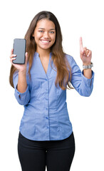 Canvas Print - Young beautiful brunette business woman showing screen of smartphone over isolated background surprised with an idea or question pointing finger with happy face, number one