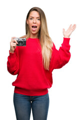 Sticker - Beautiful young woman holding vintage camera very happy and excited, winner expression celebrating victory screaming with big smile and raised hands